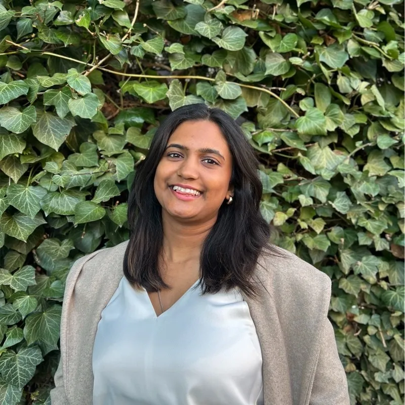 Prieyaa, founder of Nouveau Voyance, smiling in front of a wall of ivy